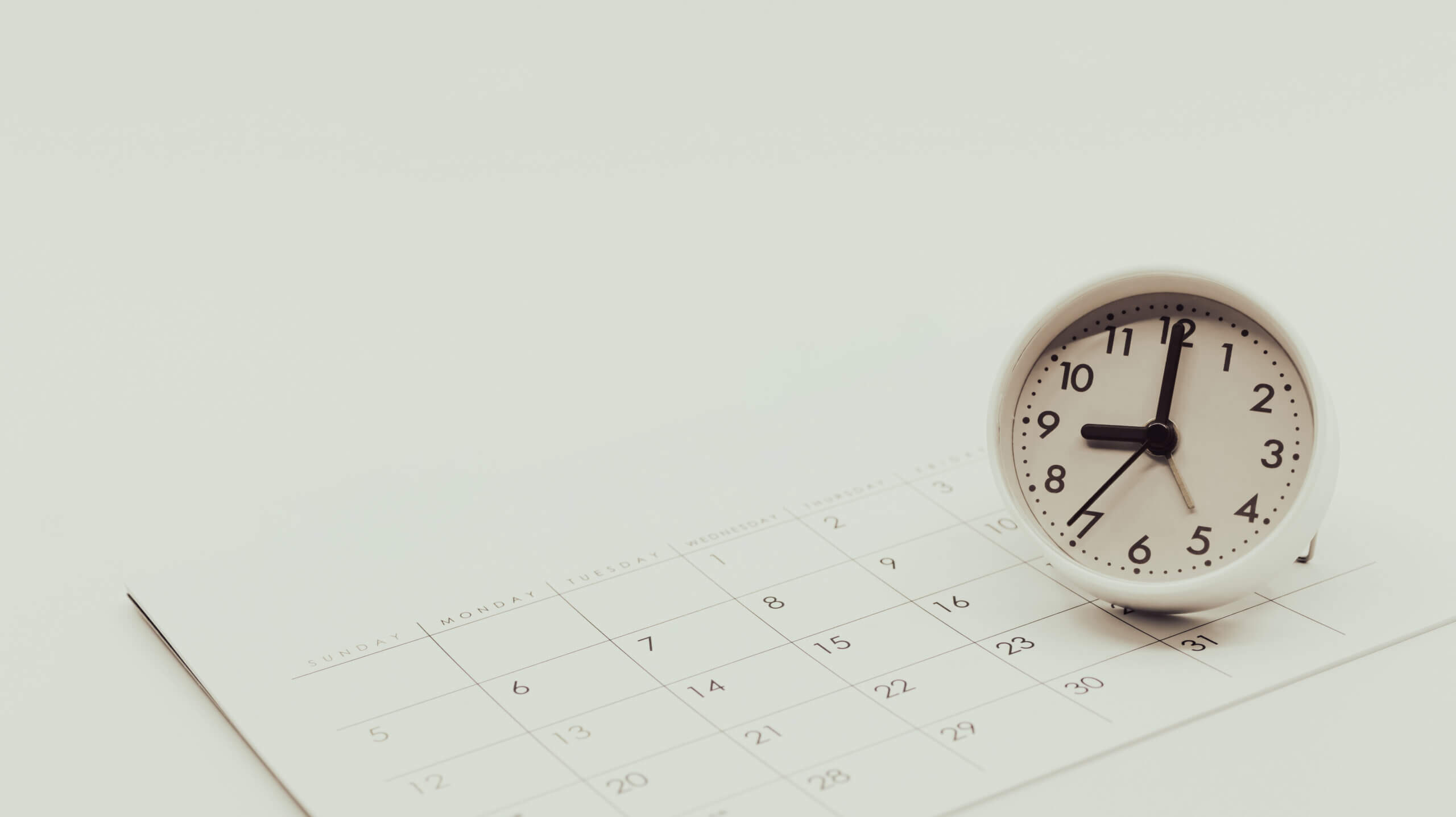 Analog clock resting on a calendar, illustrating time and date planning.
